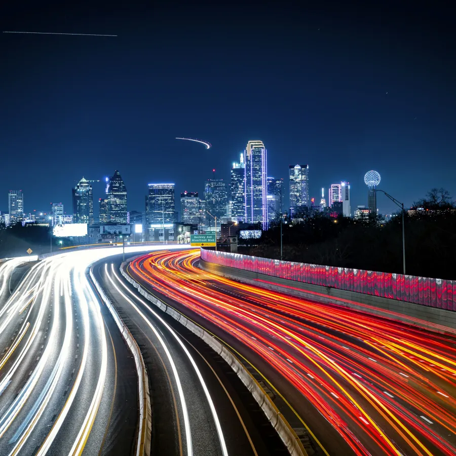 Dynamic light trails on a highway with a vibrant city skyline at night.