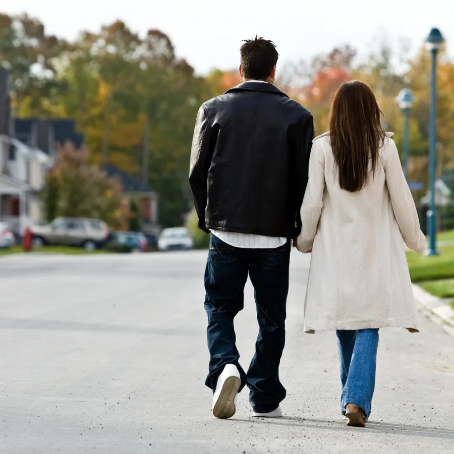 Couple walking hand in hand down a suburban street, surrounded by colorful autumn trees.