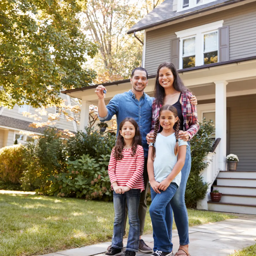 Happy family posing in front of their new home, showcasing joy and excitement of homeownership.