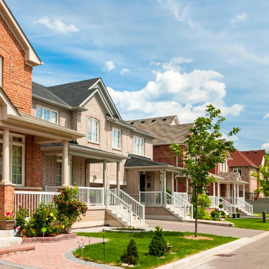 Row of modern suburban houses under a blue sky with scattered clouds, featuring lush green lawns.