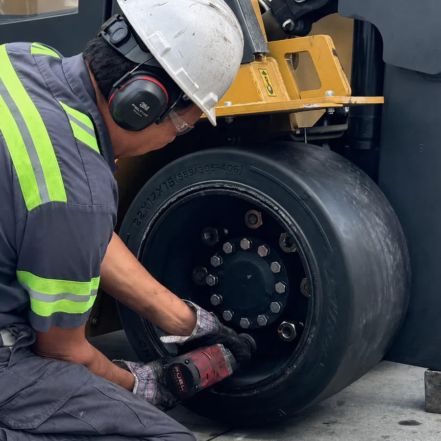 Worker in safety gear repairing or maintaining a heavy-duty forklift tire with power tool in industrial setting