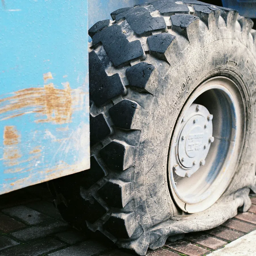 Close-up of a flat, worn-out tire on a blue industrial vehicle parked on a brick pavement.
