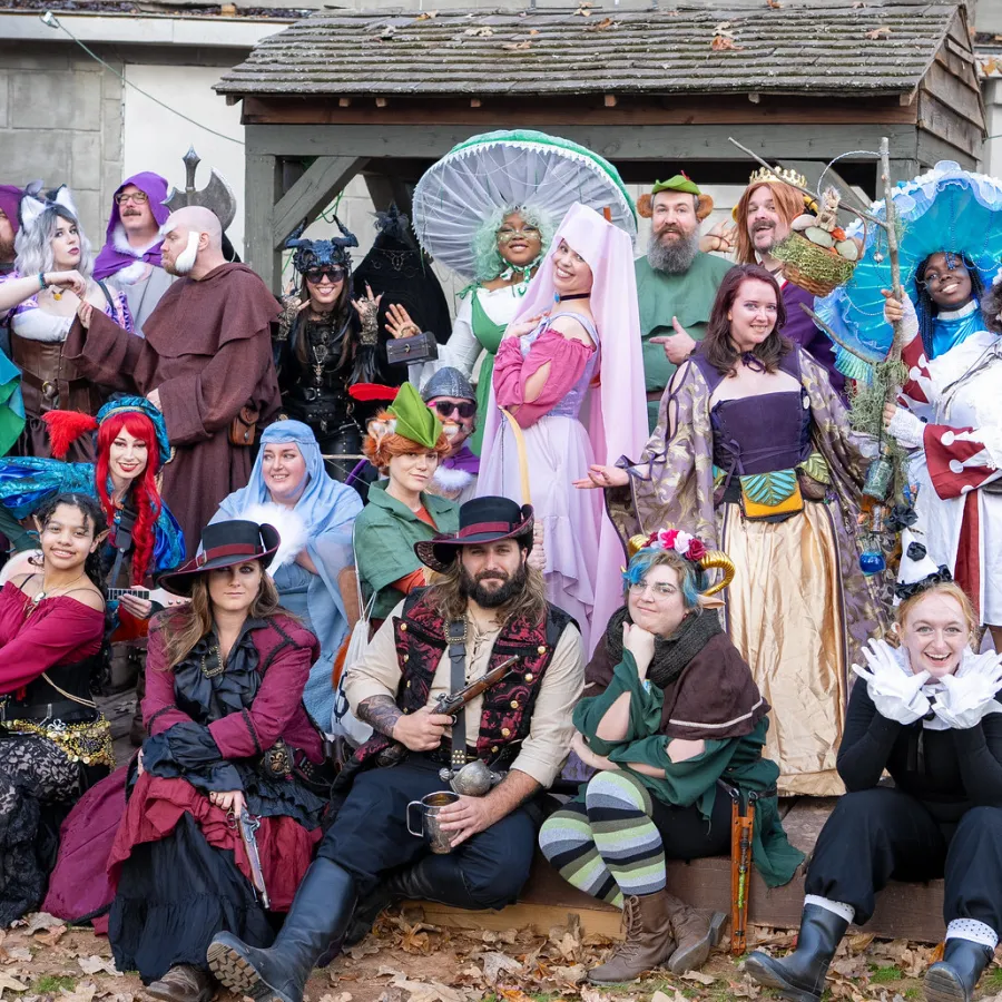 Group of people in colorful medieval and fantasy costumes posing outdoors on a bed of autumn leaves.