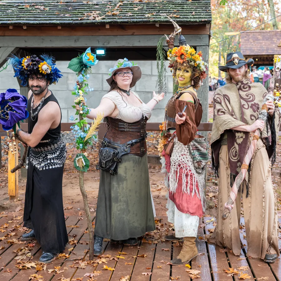 Four people in fantasy and nature-themed costumes posing at an outdoor autumn festival with a costume contest sign