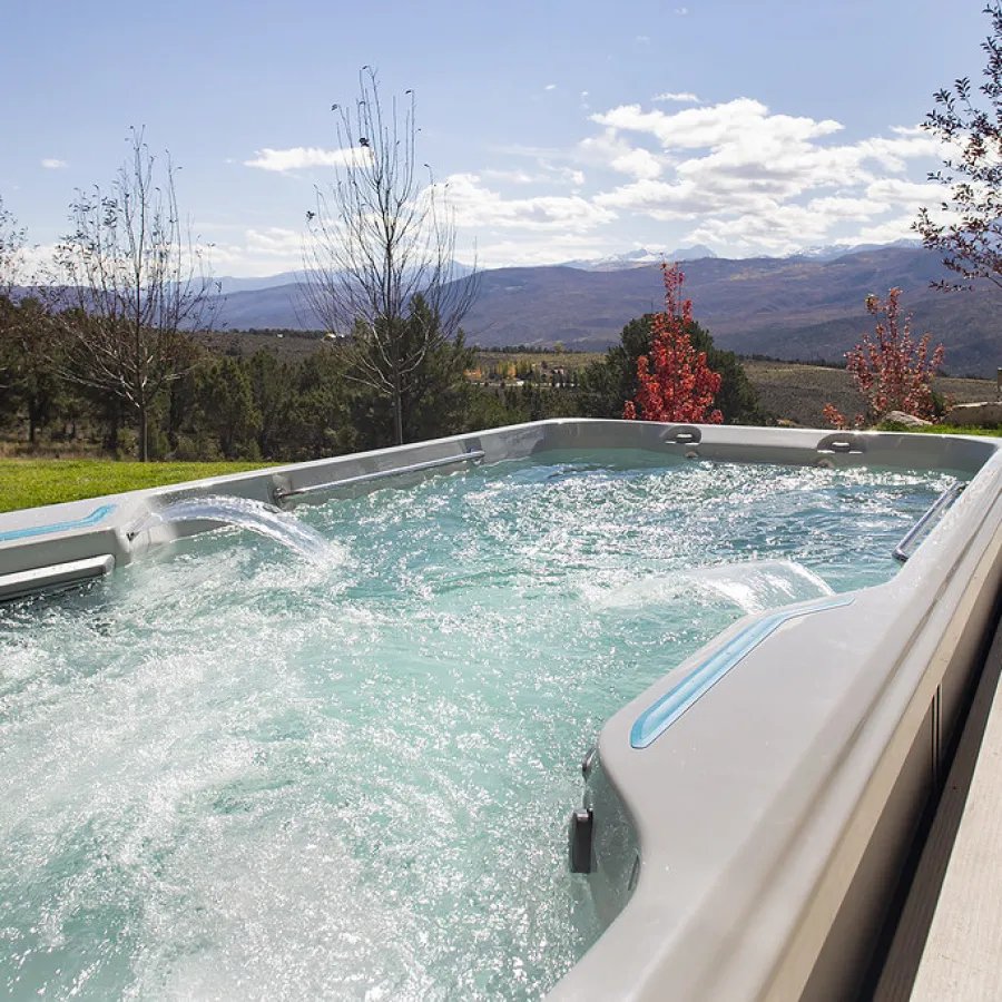 Outdoor swim spa with bubbling water and mountain view under a partly cloudy sky on a sunny day.