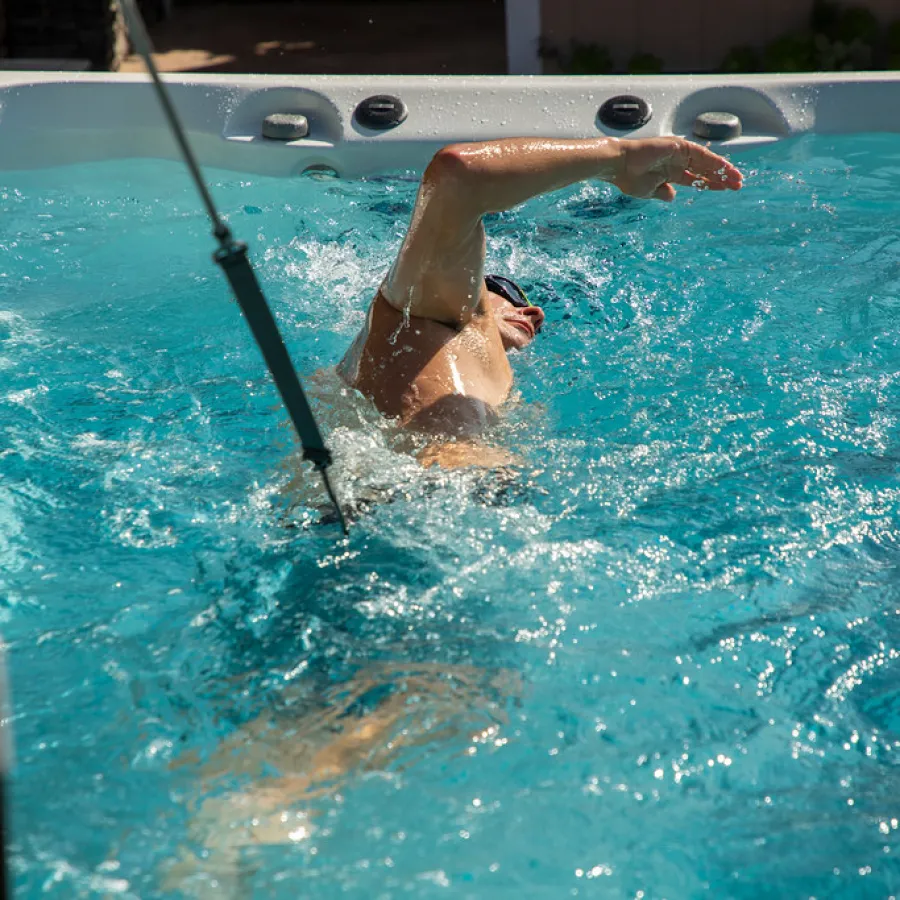 Person wearing swim goggles swimming freestyle in a clear outdoor pool with splashing water.