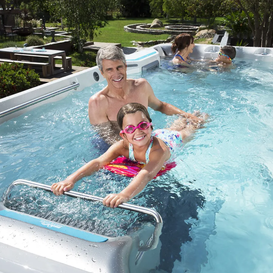 Man and child swimming and playing together in a backyard swim spa on a sunny day