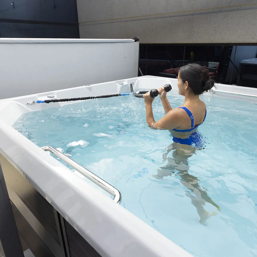 Woman in blue swimsuit exercises with water resistance bands in outdoor aquatic therapy pool.