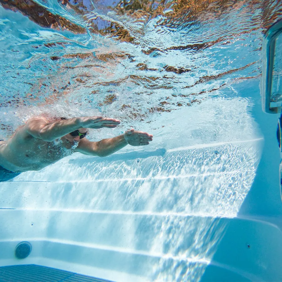 Underwater view of a man swimming freestyle in a clear pool with sunlight reflections on the water surface