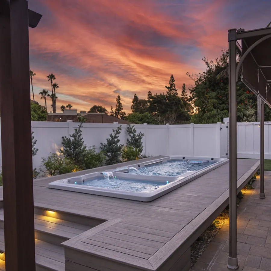 Modern backyard with illuminated swim spa at sunset surrounded by white fence and greenery