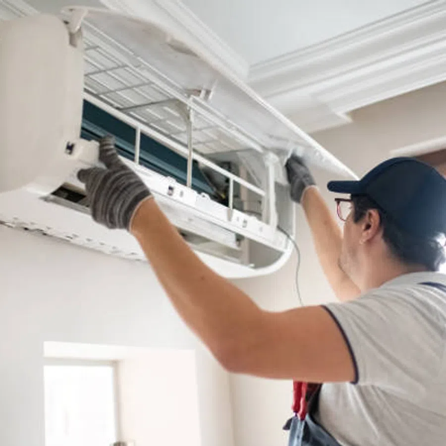 Technician wearing gloves and cap inspecting and repairing a wall-mounted air conditioning unit indoors