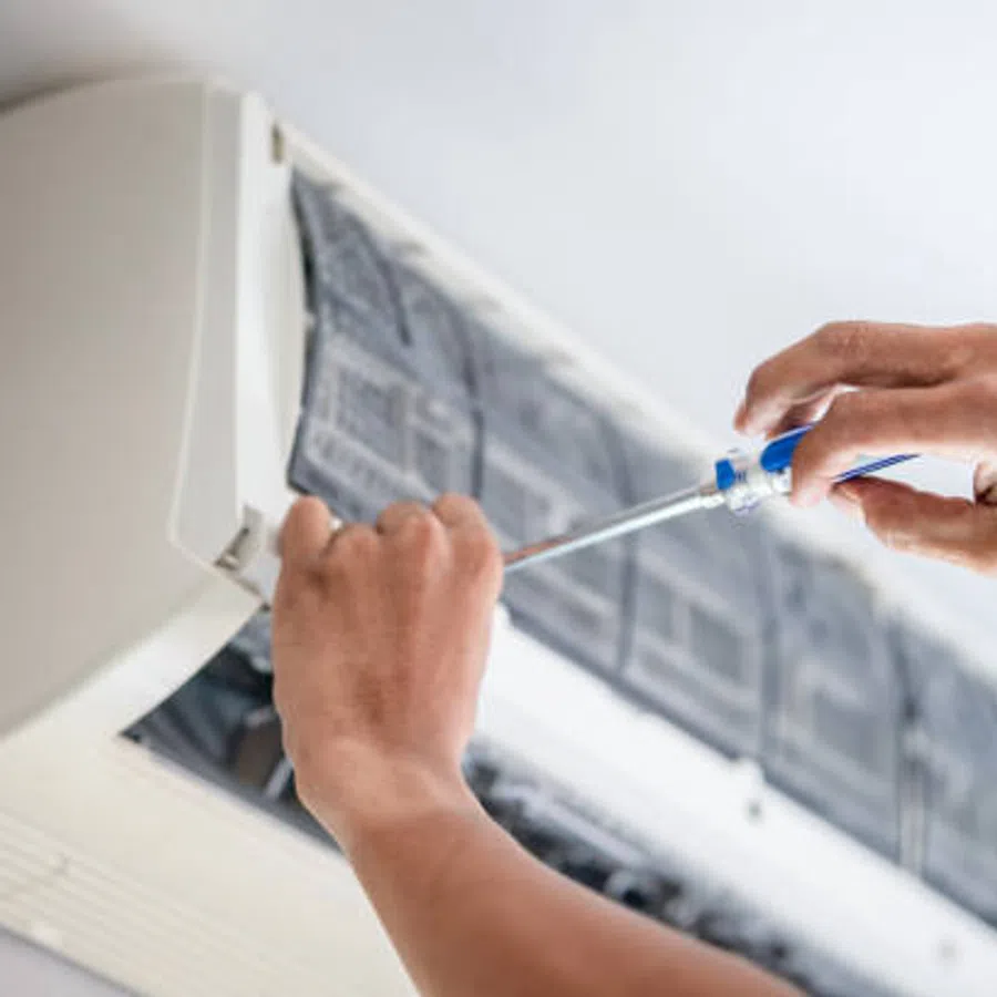Technician repairing an indoor air conditioner unit using a screwdriver on a wall-mounted split AC system.