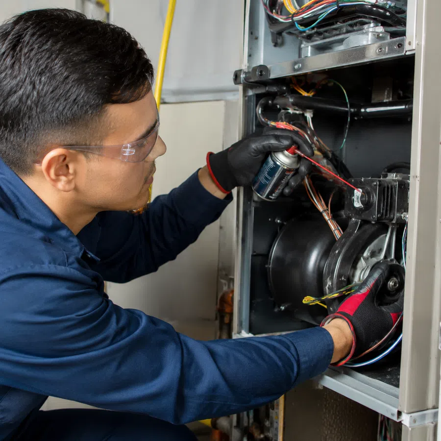 Technician wearing safety glasses and gloves repairing and spraying lubricant inside HVAC unit