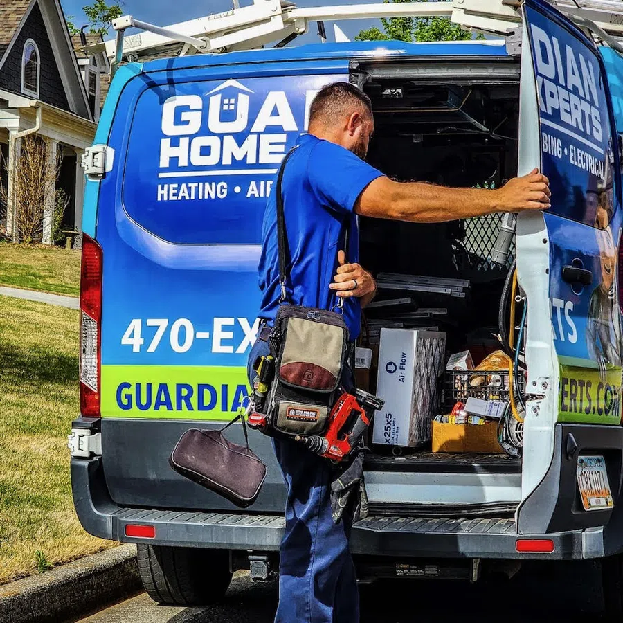 Technician in blue uniform unloading tools from a Guardian Homes service van in a residential neighborhood.