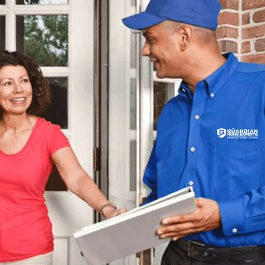 Female homeowner greets male service technician in blue uniform holding clipboard at front door
