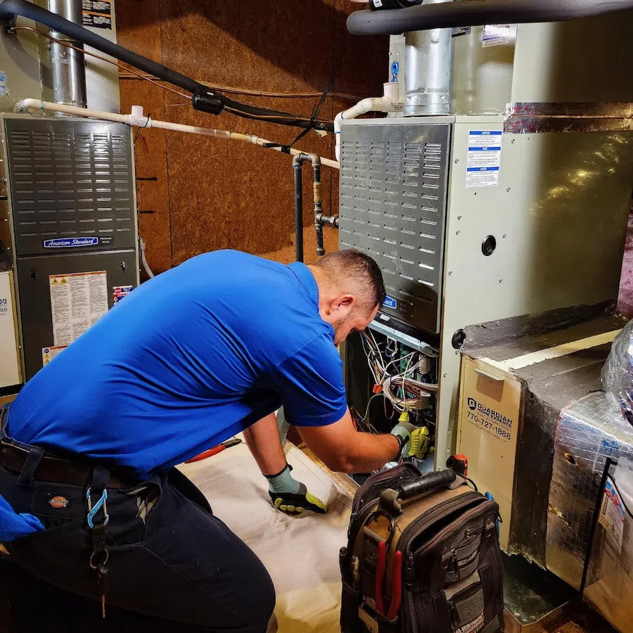 Technician in blue shirt repairing HVAC furnace system in a basement with tools and equipment nearby