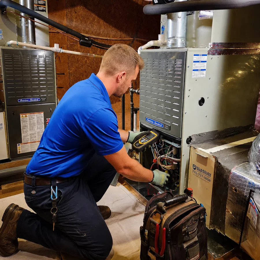 HVAC technician in blue shirt diagnosing furnace system with electronic device in a basement setting.