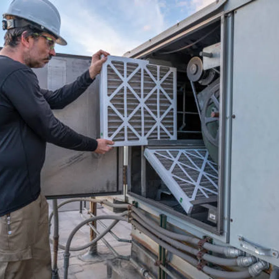 Technician in safety helmet installing or replacing HVAC air filters on rooftop unit during maintenance