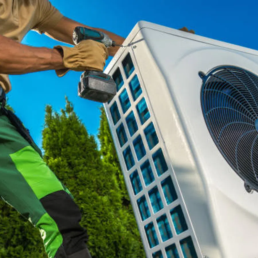 Technician repairing or installing an outdoor air conditioning unit on a sunny day with green trees in the background