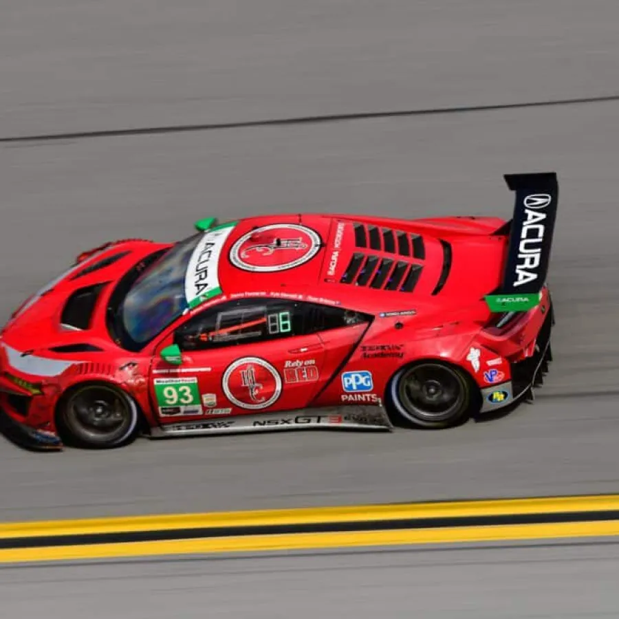 Red Acura NSX race car with number 93 speeding on racetrack with yellow dividing lines visible.