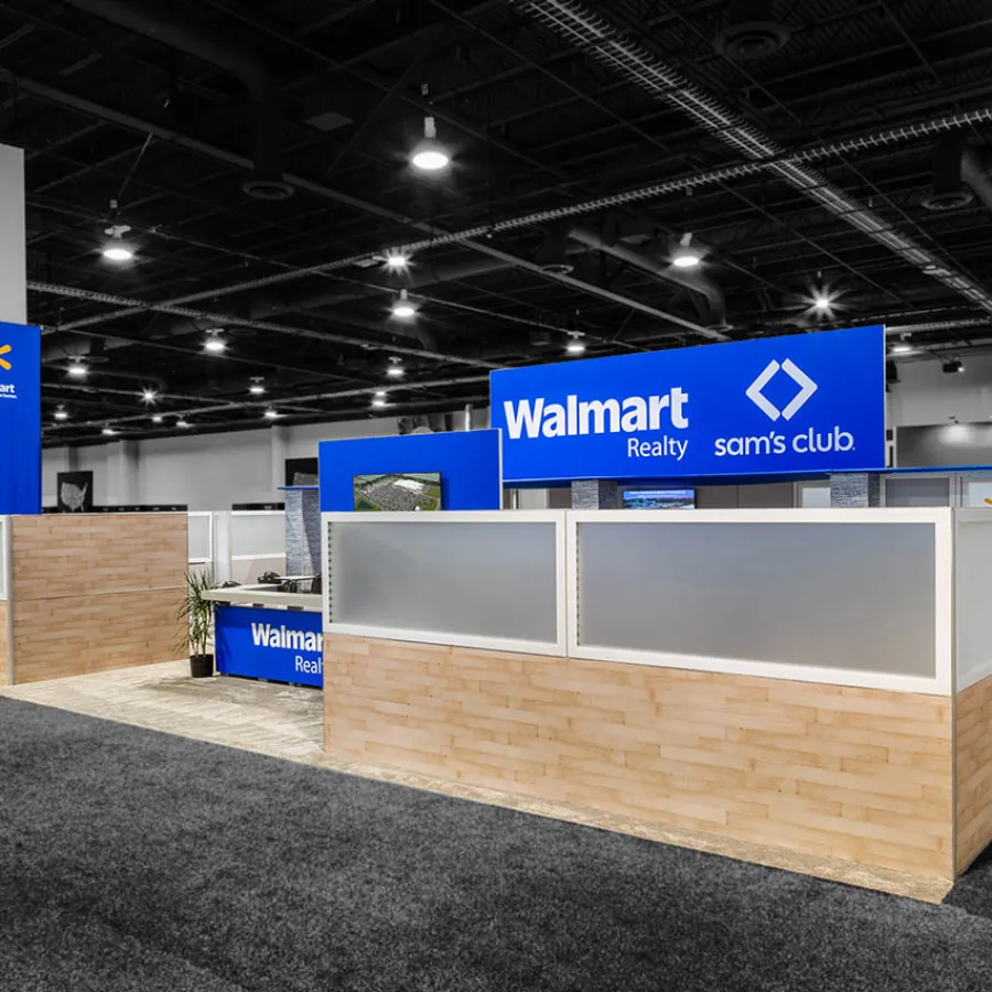 Walmart Realty and Sam's Club booth with blue signage and wood-paneled partitions in large conference hall.