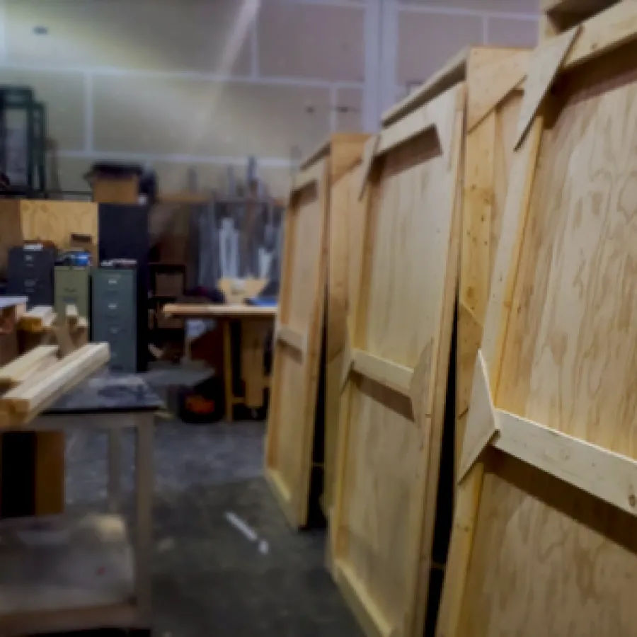 Wooden crates and lumber pieces in a woodworking workshop with tools and storage in the background.