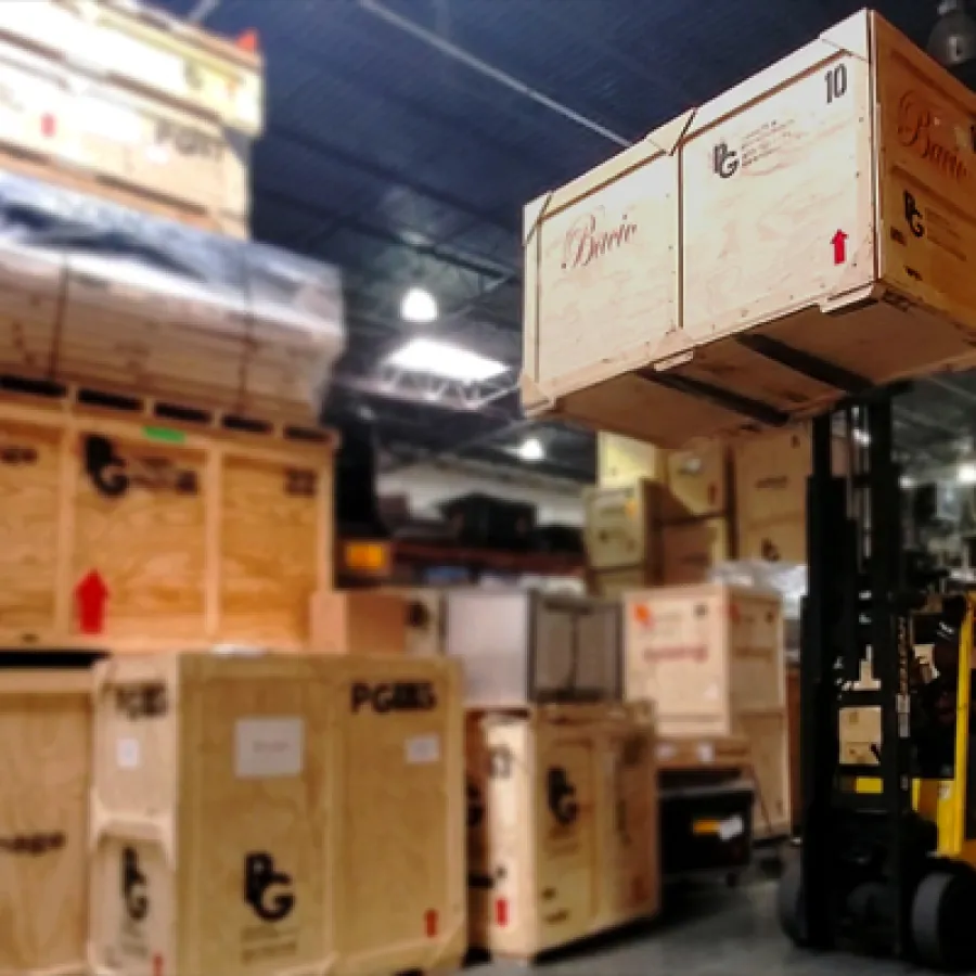 Forklift lifting large wooden crate in a warehouse filled with stacked wooden shipping boxes under bright lights