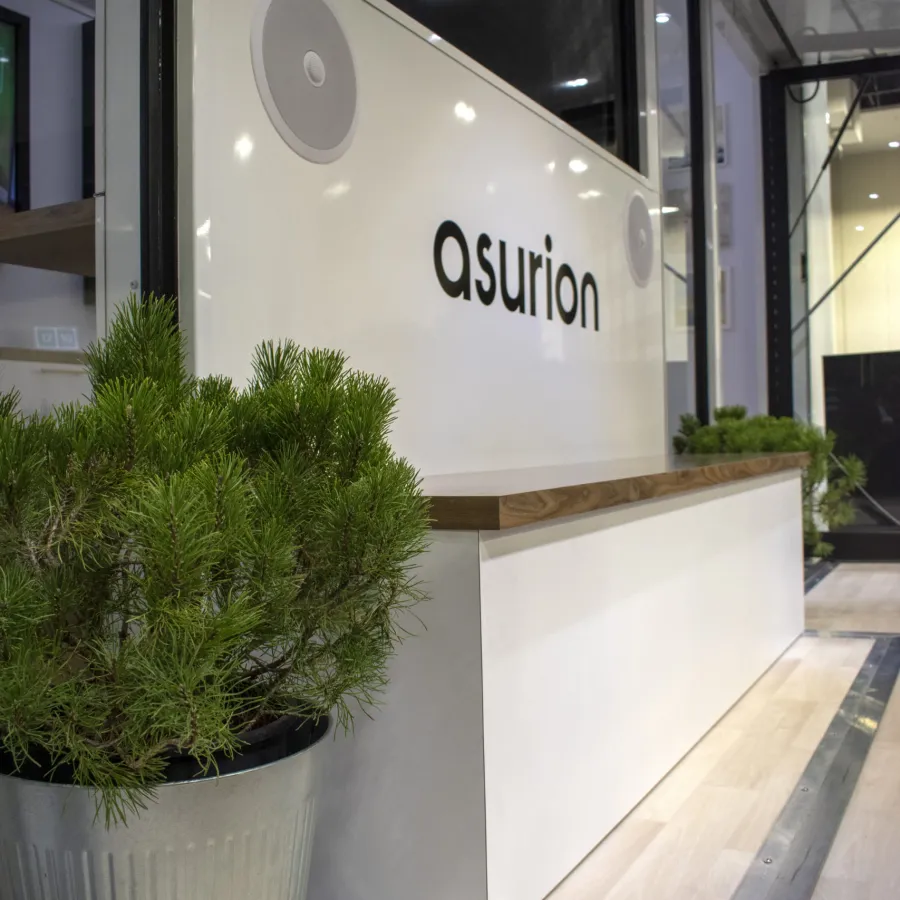 Modern office reception area with Asurion logo, white desk, wooden countertop, and green plant in metal pot.