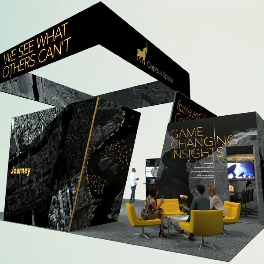 Modern exhibition booth with black walls, yellow accents, and text highlighting insights and journey, people seated and interacting.