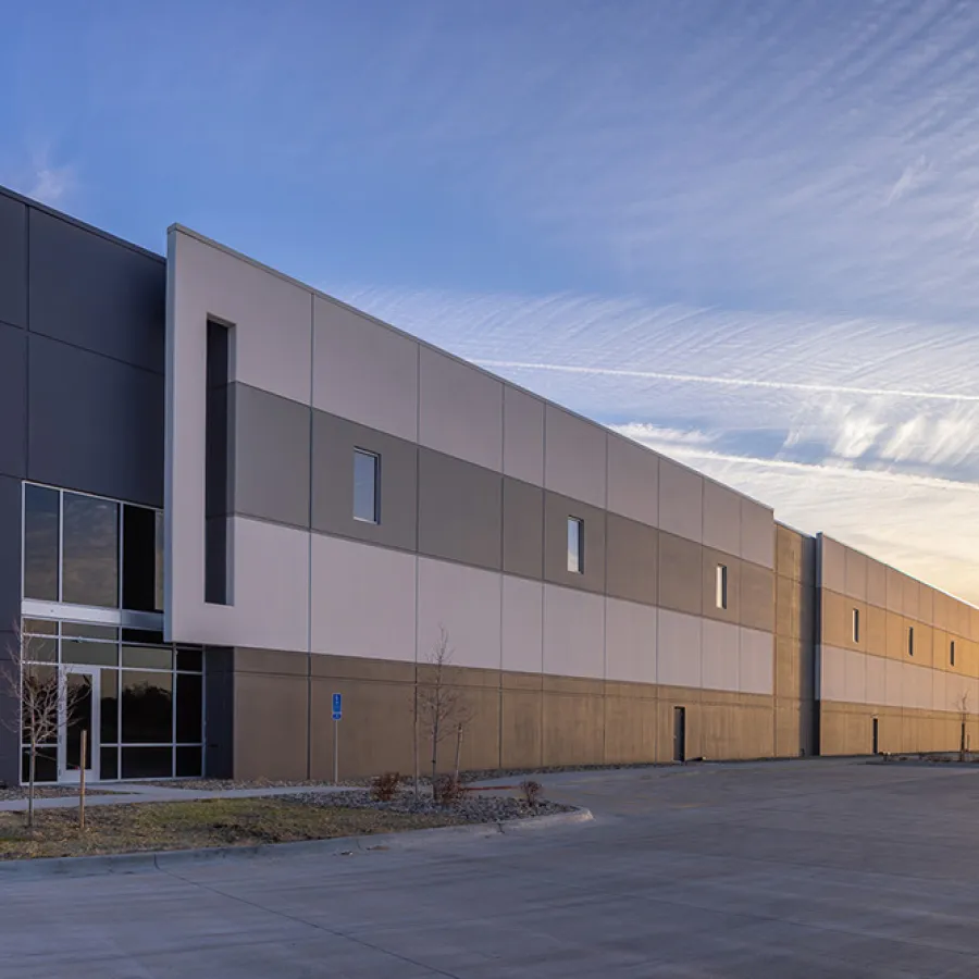 Modern industrial warehouse building with large gray panels and wide driveway under a clear sky at sunset.