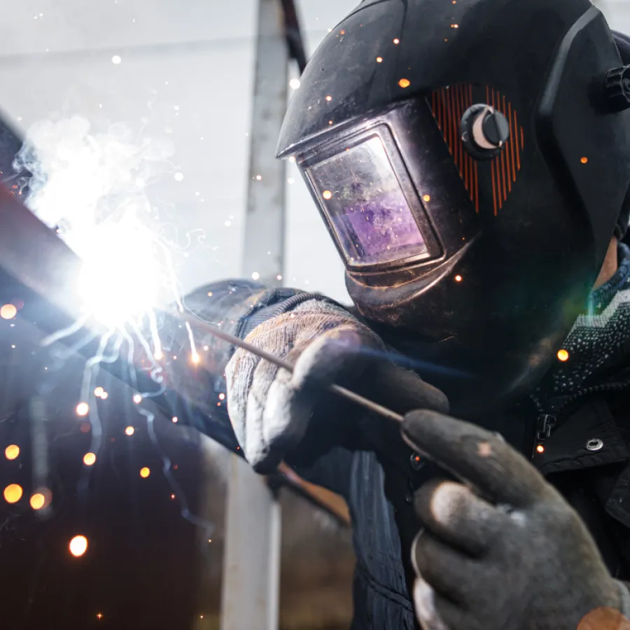 Welder wearing protective helmet and gloves using welding rod with bright sparks flying around