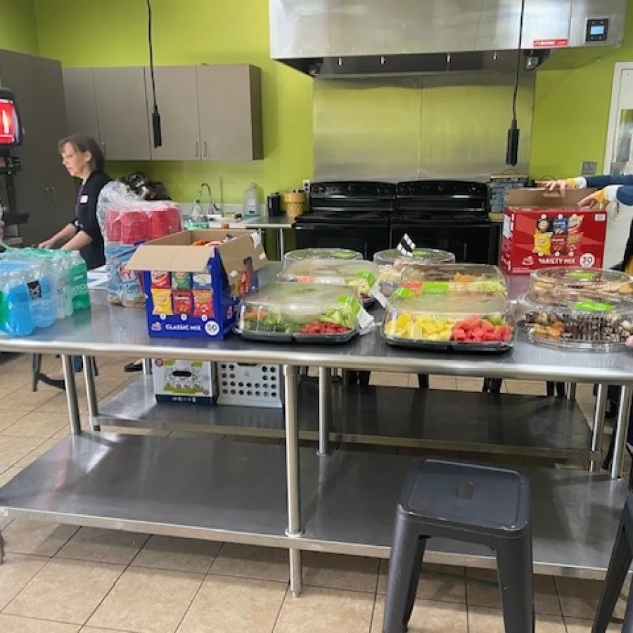 a group of people stand around a table full of food