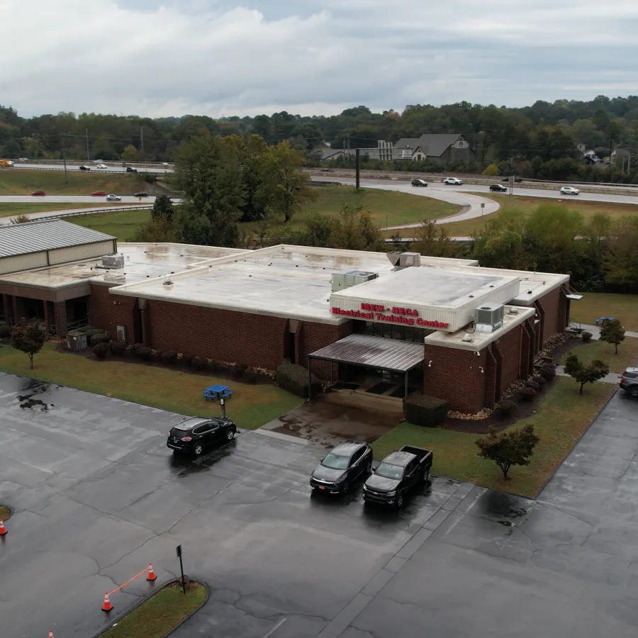 Aerial view of a single-story brick medical center building with a wet parking lot and several cars on a cloudy day.