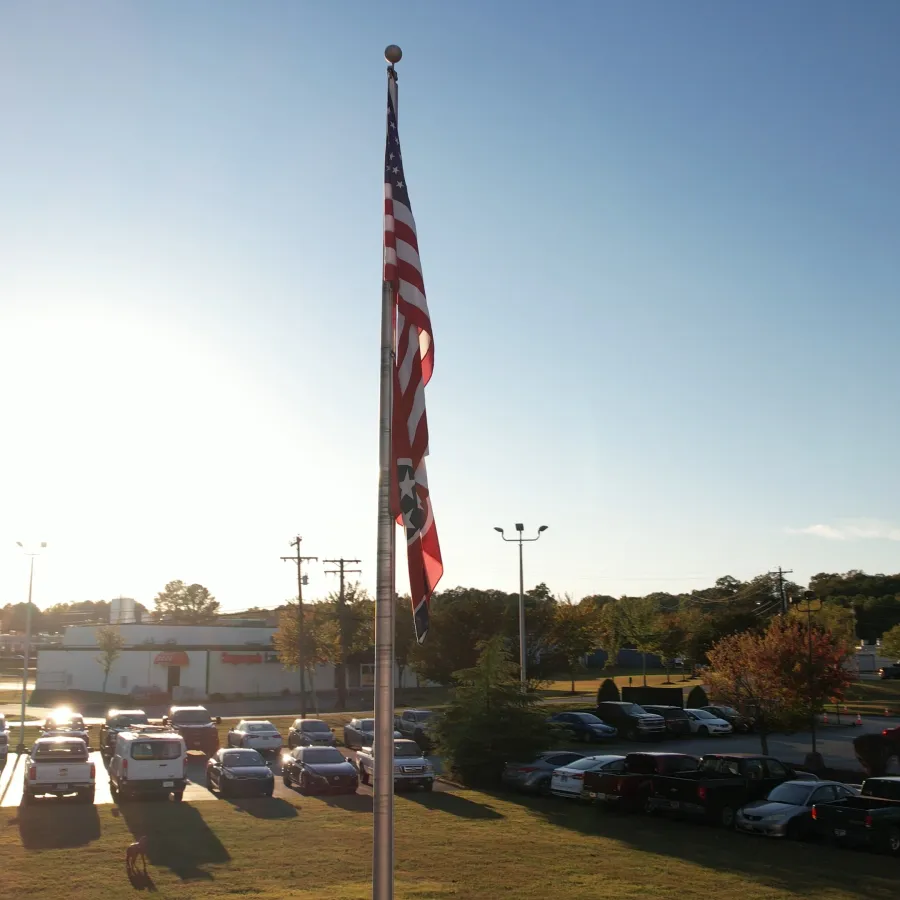 American flag on a flagpole overlooking a large parking lot with vehicles at sunset under clear sky