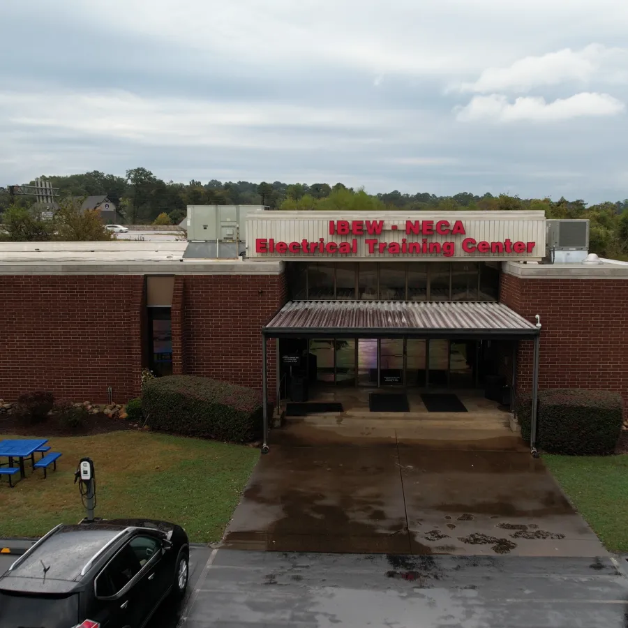 Brick building of IBEW-NECA Electrical Training Center with cars parked in front on a cloudy day.