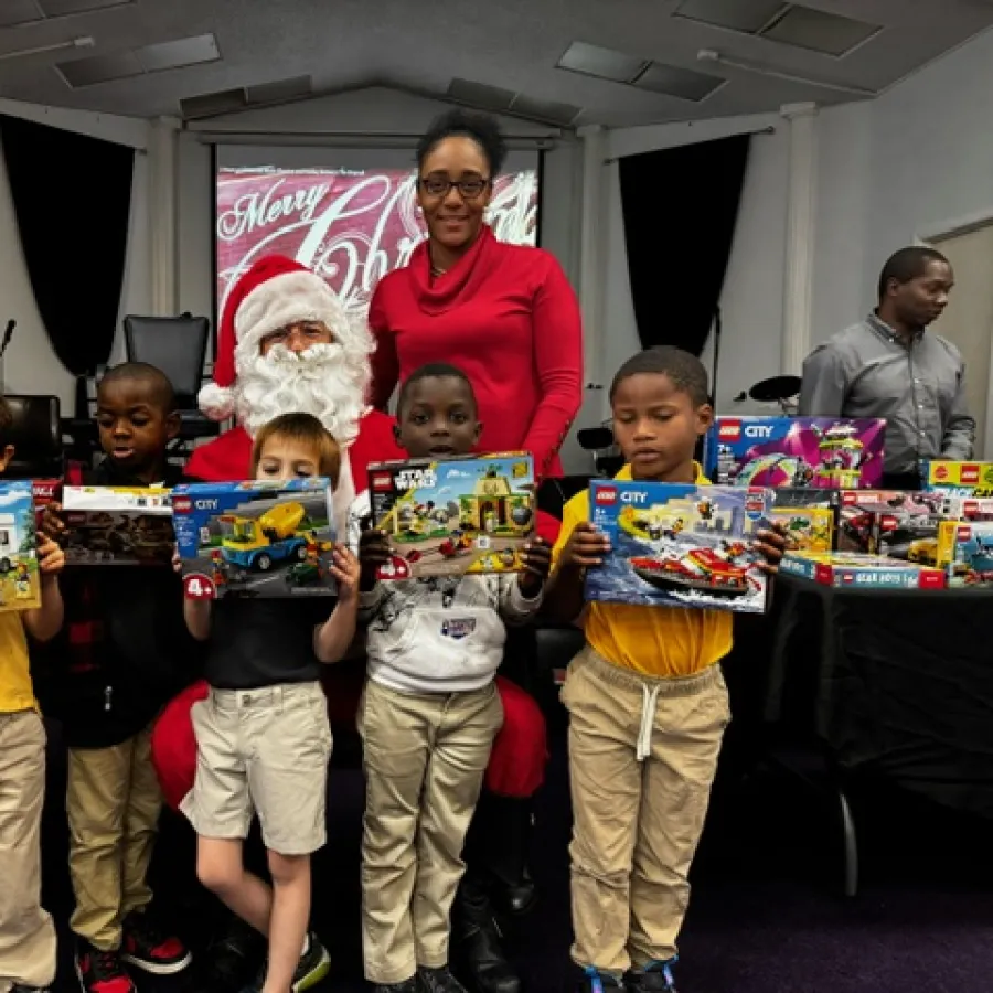 Children holding LEGO sets with Santa Claus and adults in background during Christmas event