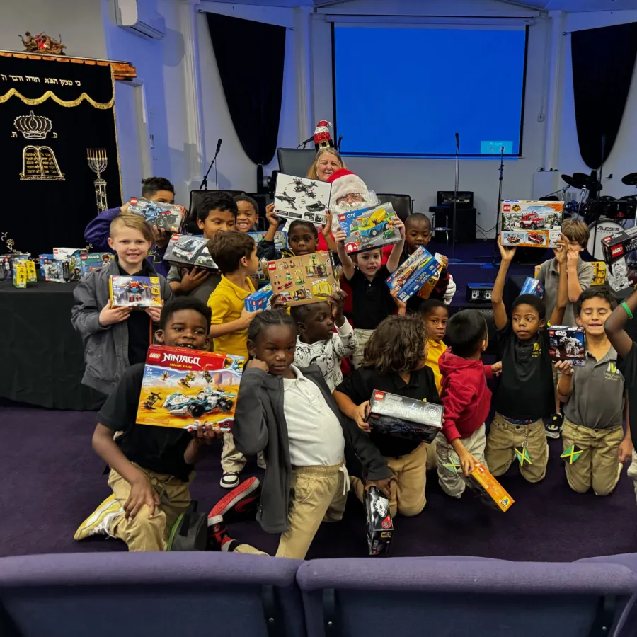 Group of joyful children holding up new LEGO sets during a holiday event with festive decorations indoors.