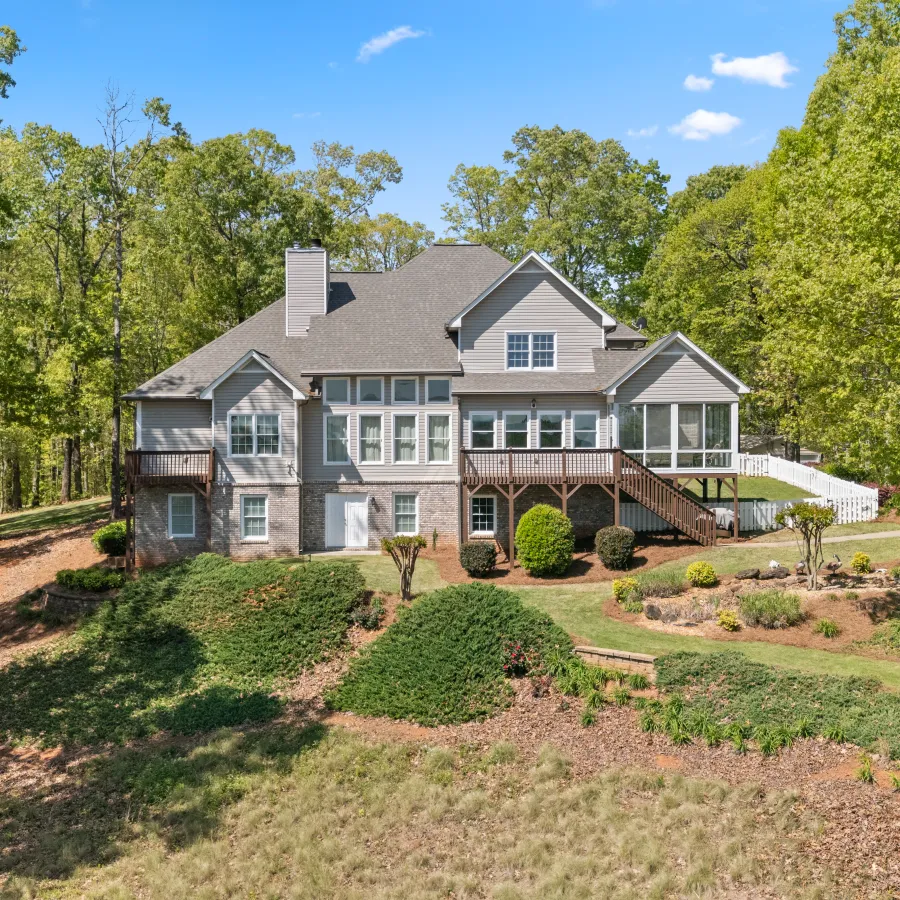 Spacious two-story house surrounded by lush green trees under a clear blue sky on a sunny day