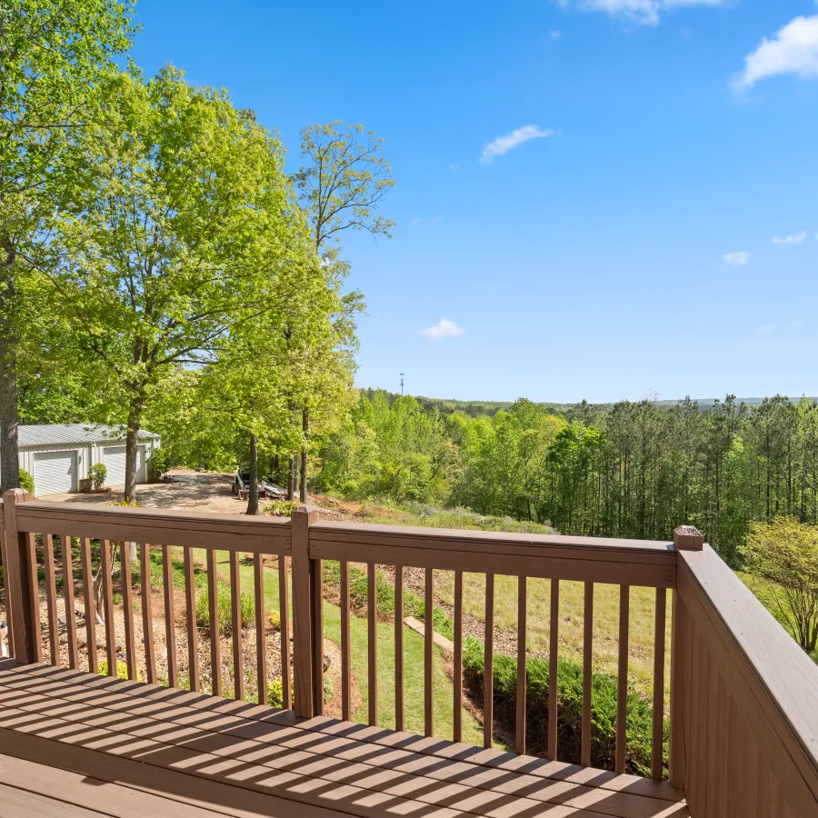 View from wooden deck overlooking lush green trees and hills under a clear blue sky on a sunny day