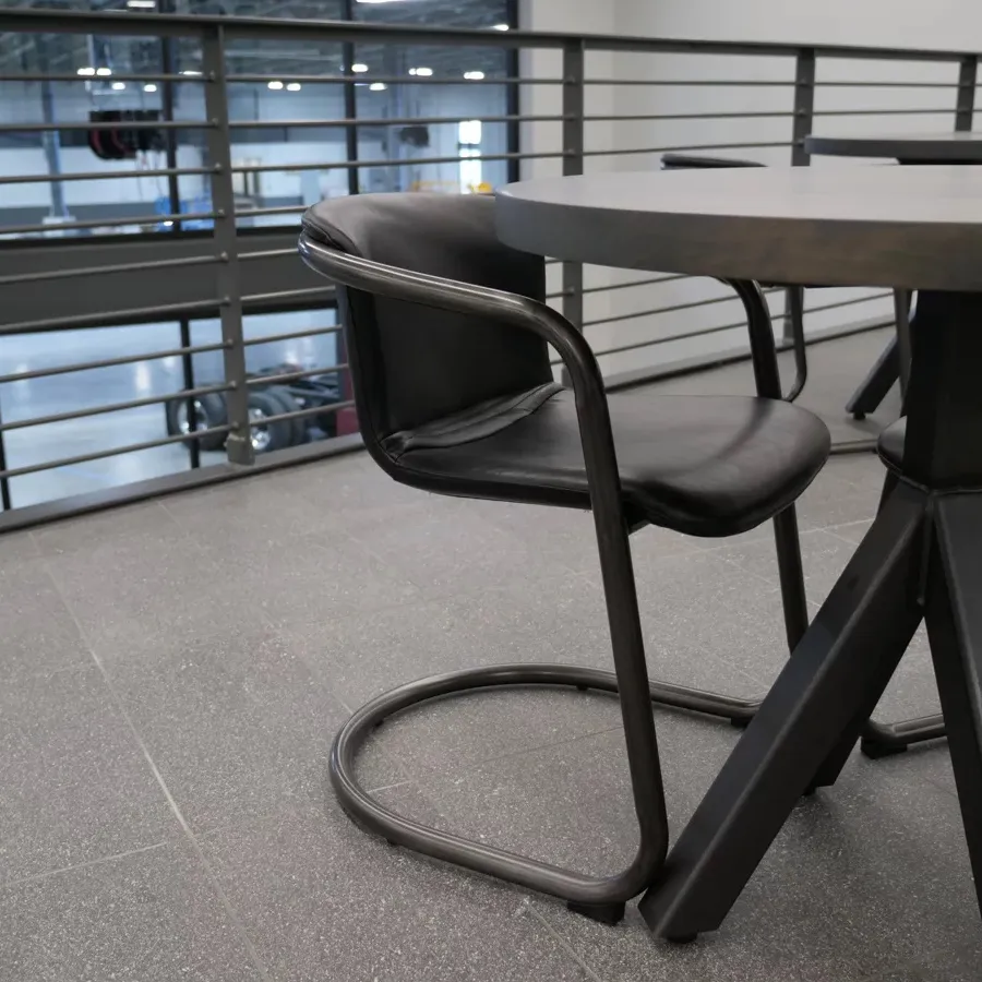 Modern black chair with curved metal frame beside a round black table in a minimalist indoor setting.