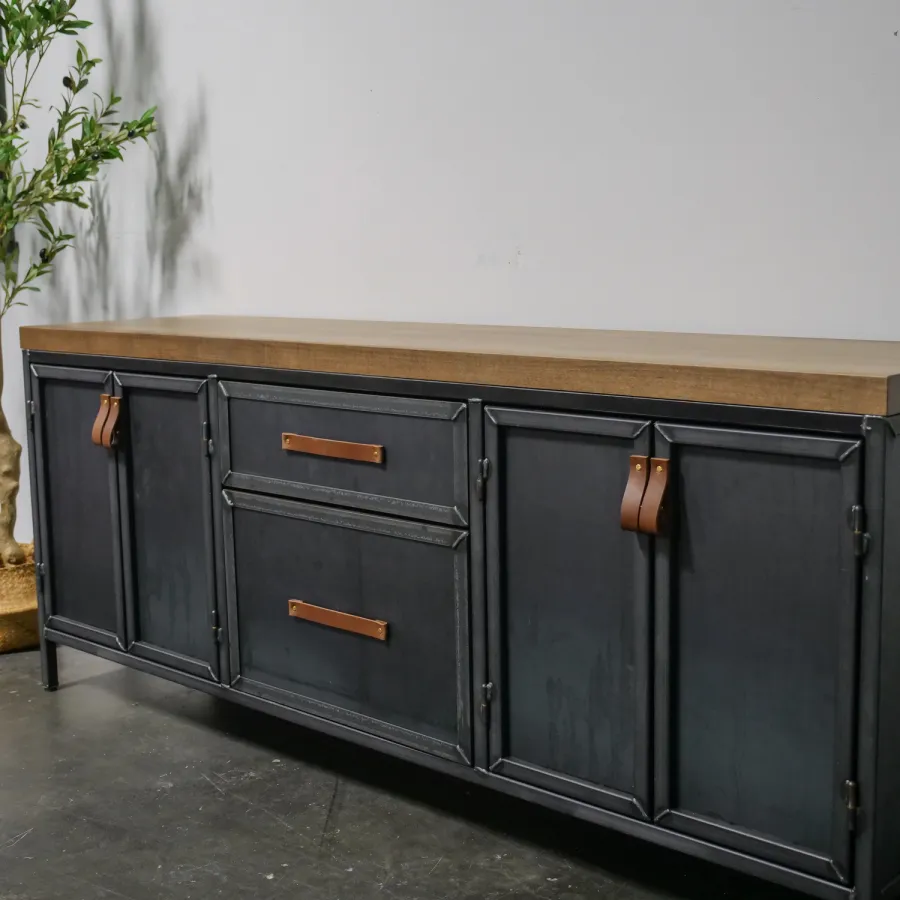 Industrial style black metal sideboard with wooden top and leather handles, next to a potted tree indoors.