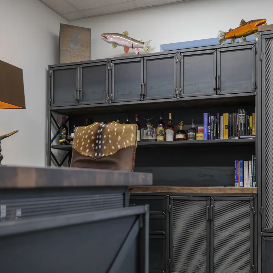 Modern office with dark metal cabinets, wooden desk, leather chair with animal print throw, and decorative lamps.