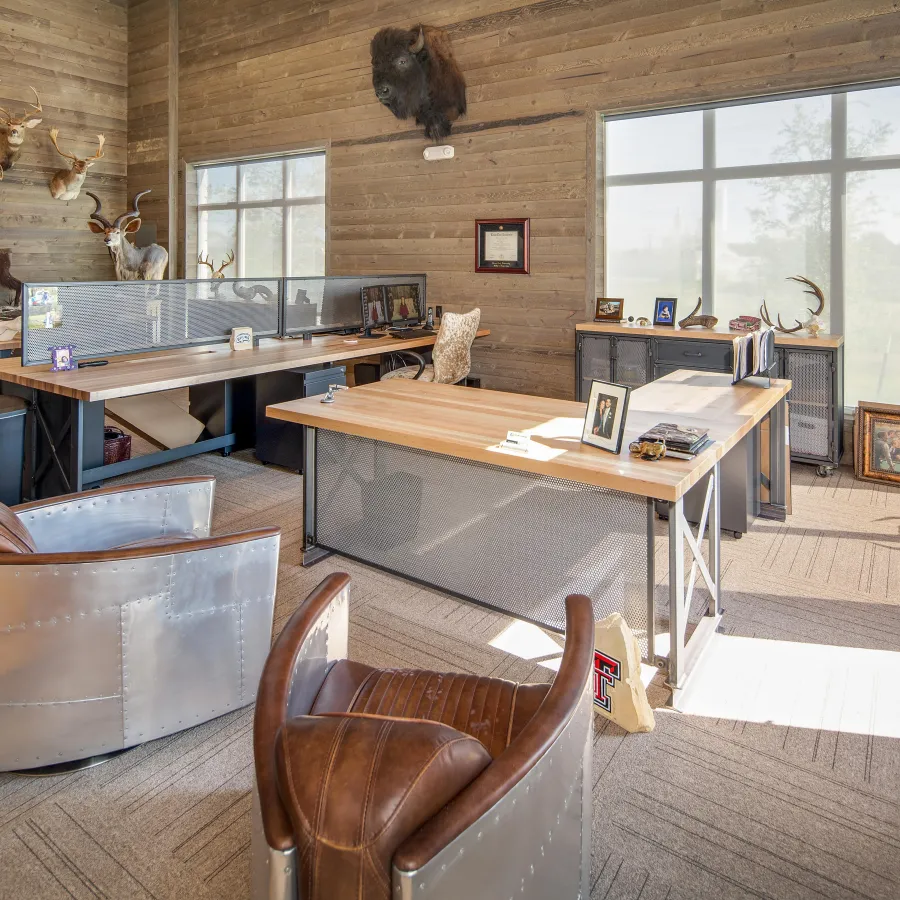 Rustic office with wood walls, metal and leather chairs, mounted animal heads, and large windows letting in natural light