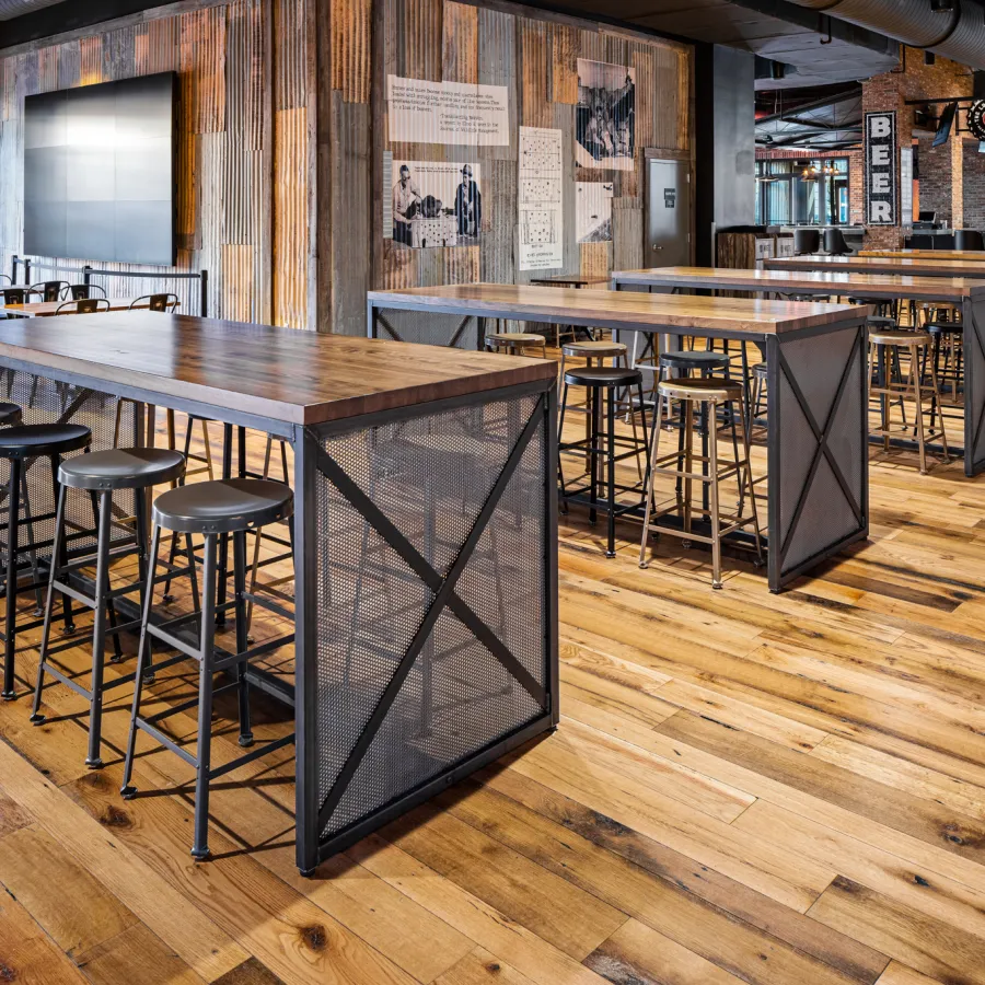 Industrial style restaurant interior with long wooden tables, metal stools, and rustic hardwood floors.