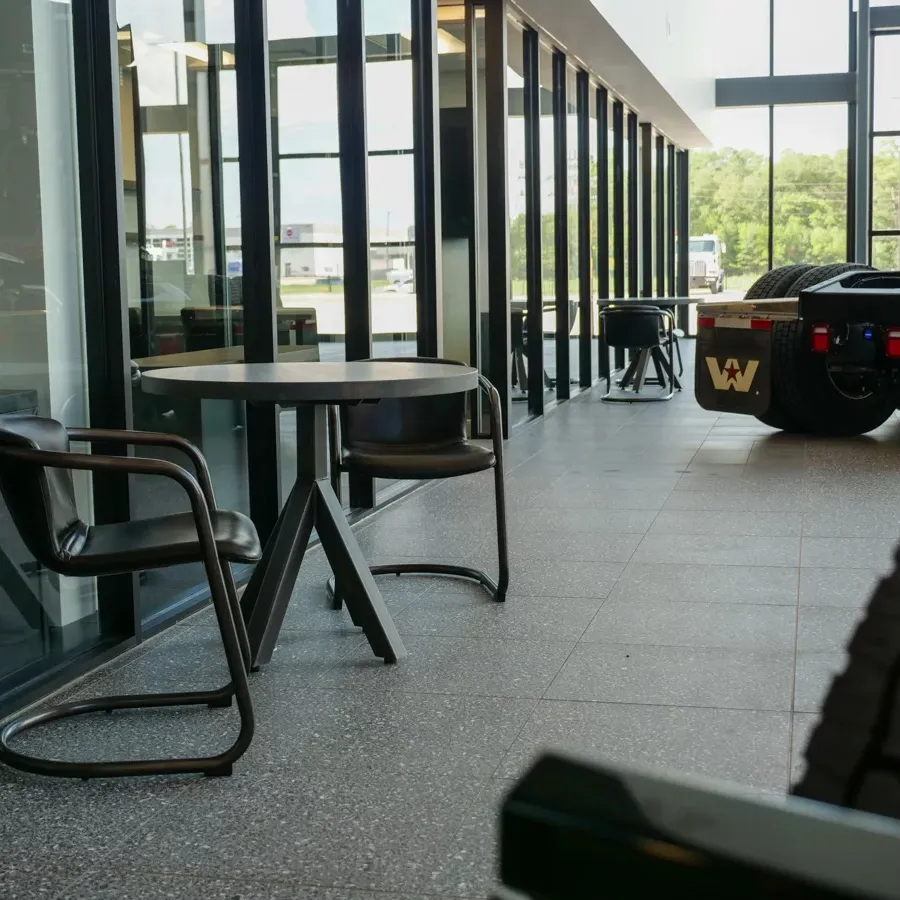 Modern indoor seating area with round table and chairs next to large windows in a truck showroom.