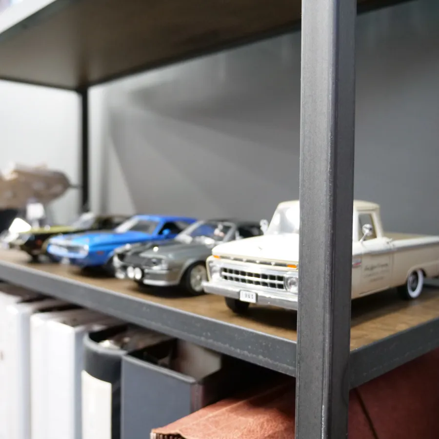 Close-up of detailed vintage model cars and a white pickup truck displayed on a wooden shelf with books below.