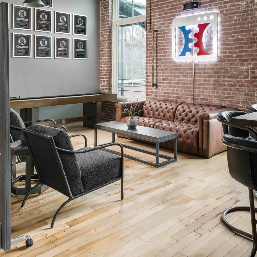 Modern lounge area with brown leather sofa, black armchairs, wooden coffee table, and framed art on brick wall