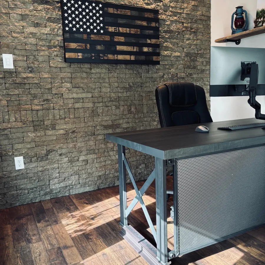 Modern office with stone brick wall, industrial desk, black chair, and wooden American flag decor.