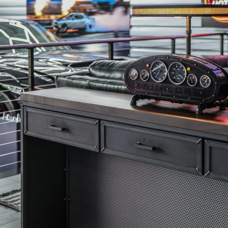 Modern black desk with vintage car dashboard clock and leather couch in stylish garage setting