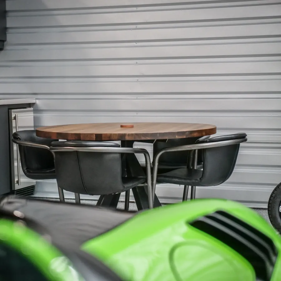 Modern garage with round wooden table, black chairs, green car hood, and storage cabinets